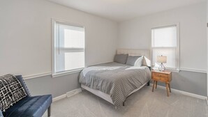 Een slaapkamer met een bed, nachtkastje, lamp en stoel.
