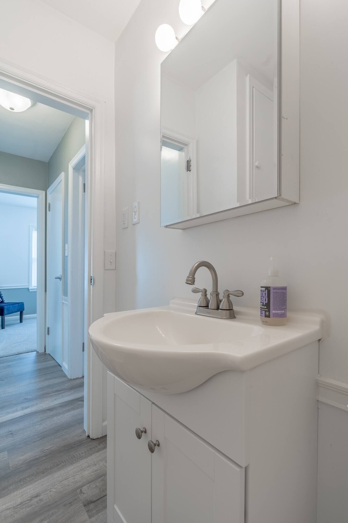 A bathroom with a white sink, a mirror, and a bottle of hand soap.