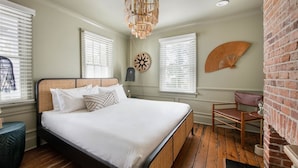 A bedroom with a large bed, a wooden floor, and a brick wall. - Ivy Manor | DT Oasis + Carriage House! (Charleston)