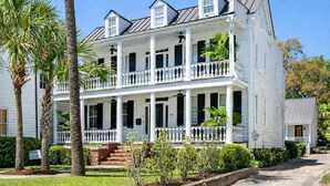 A two-story white colonial-style house with a balcony on the second floor, surrounded by palm trees and a well-maintained lawn. - Ivy Manor | DT Oasis + Carriage House! (Charleston)