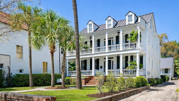 A two-story white building with a balcony, surrounded by palm trees and a brick wall. - Ivy Manor | DT Oasis + Carriage House! (Charleston)