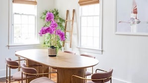 Ein Essbereich mit einem runden Tisch, sechs Stühlen, einer Topfpflanze mit violetten Blüten und Holzbalken an der Decke.