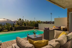Relax by the serene pool surrounded by lush greenery and palm trees, with a comfortable seating area to enjoy the view.