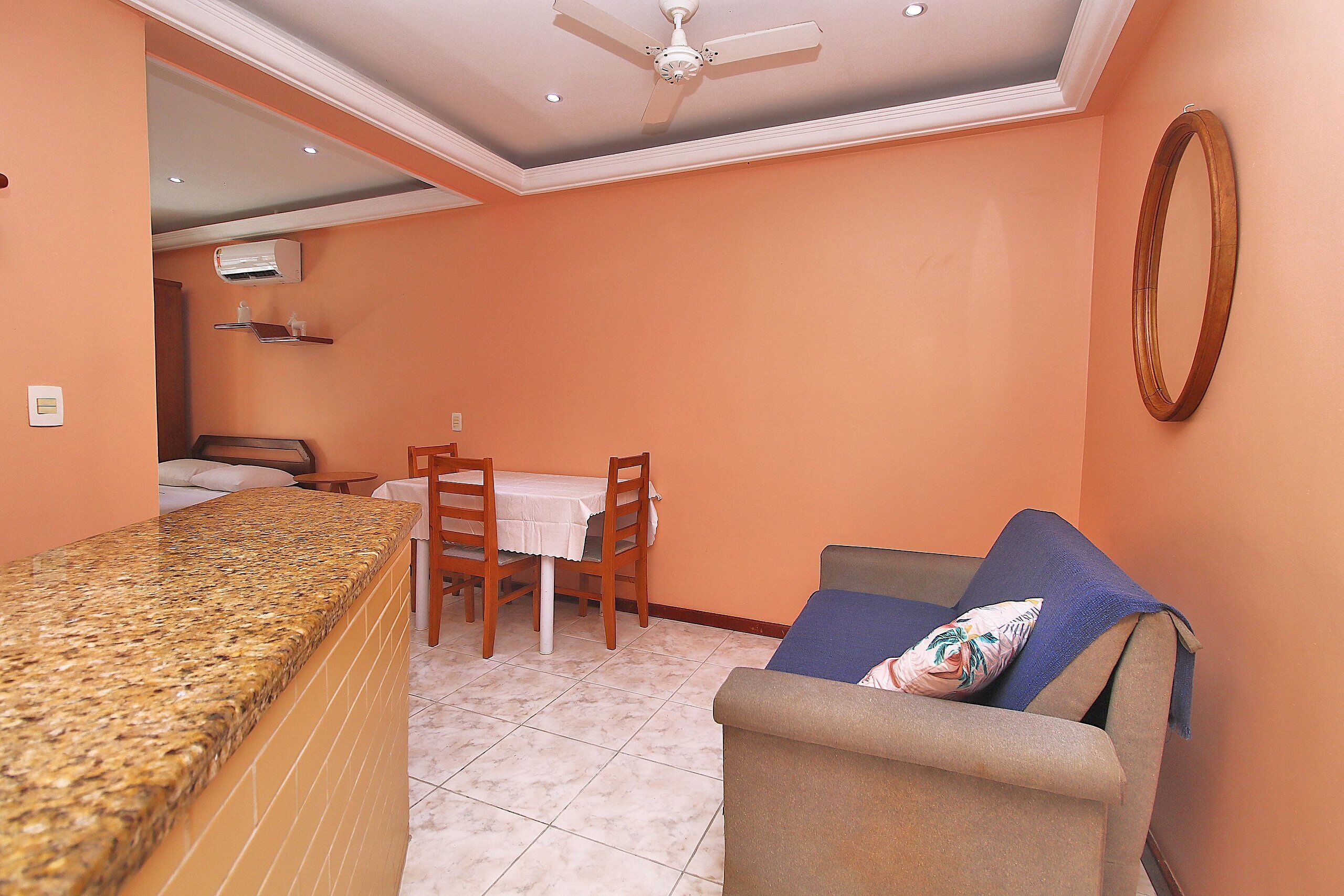 A hotel room with a kitchenette, a dining area with a table and chairs, a sofa with a pillow, and a ceiling fan.