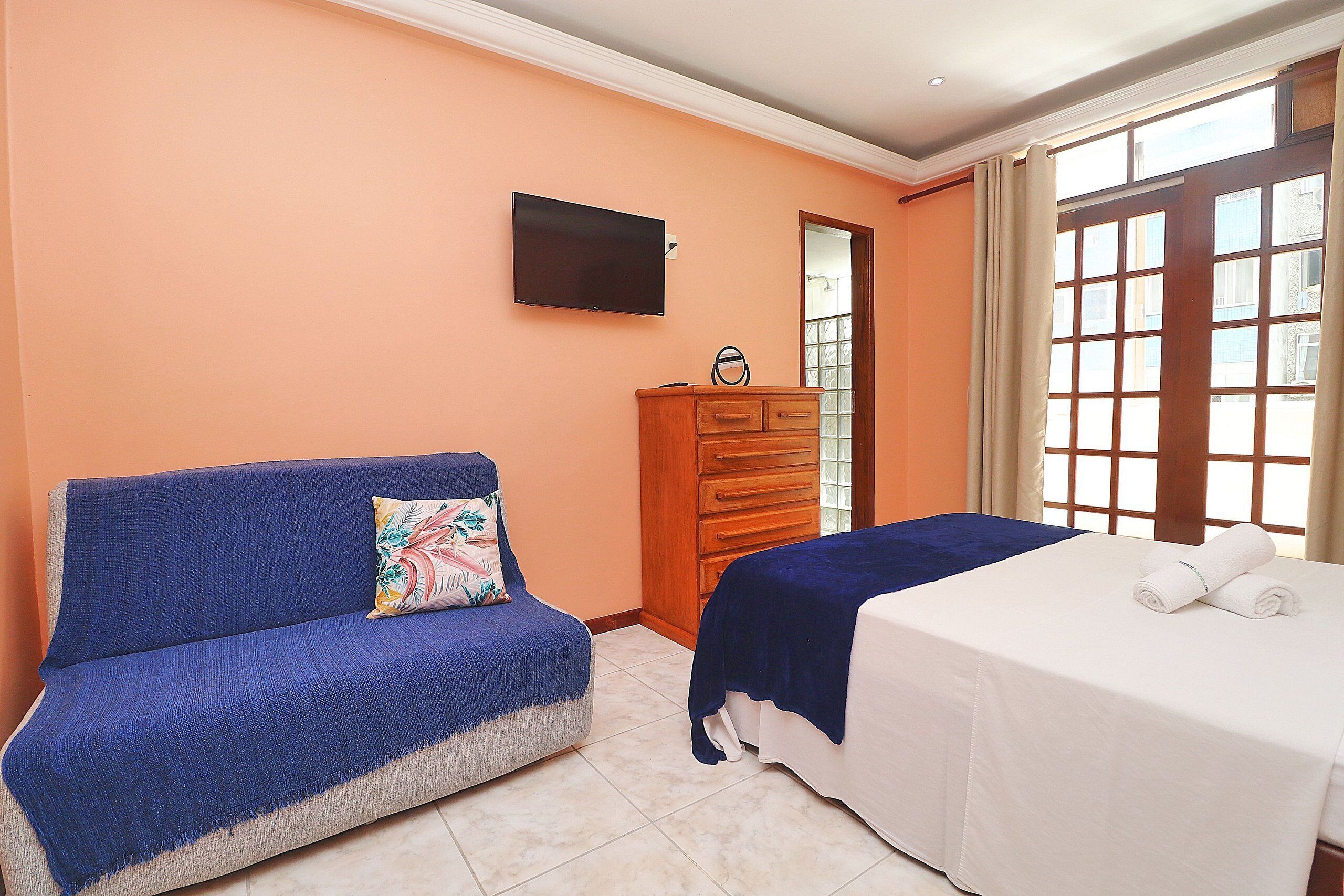 A room with a sofa, a bed, a wooden dresser, and a TV mounted on the wall.