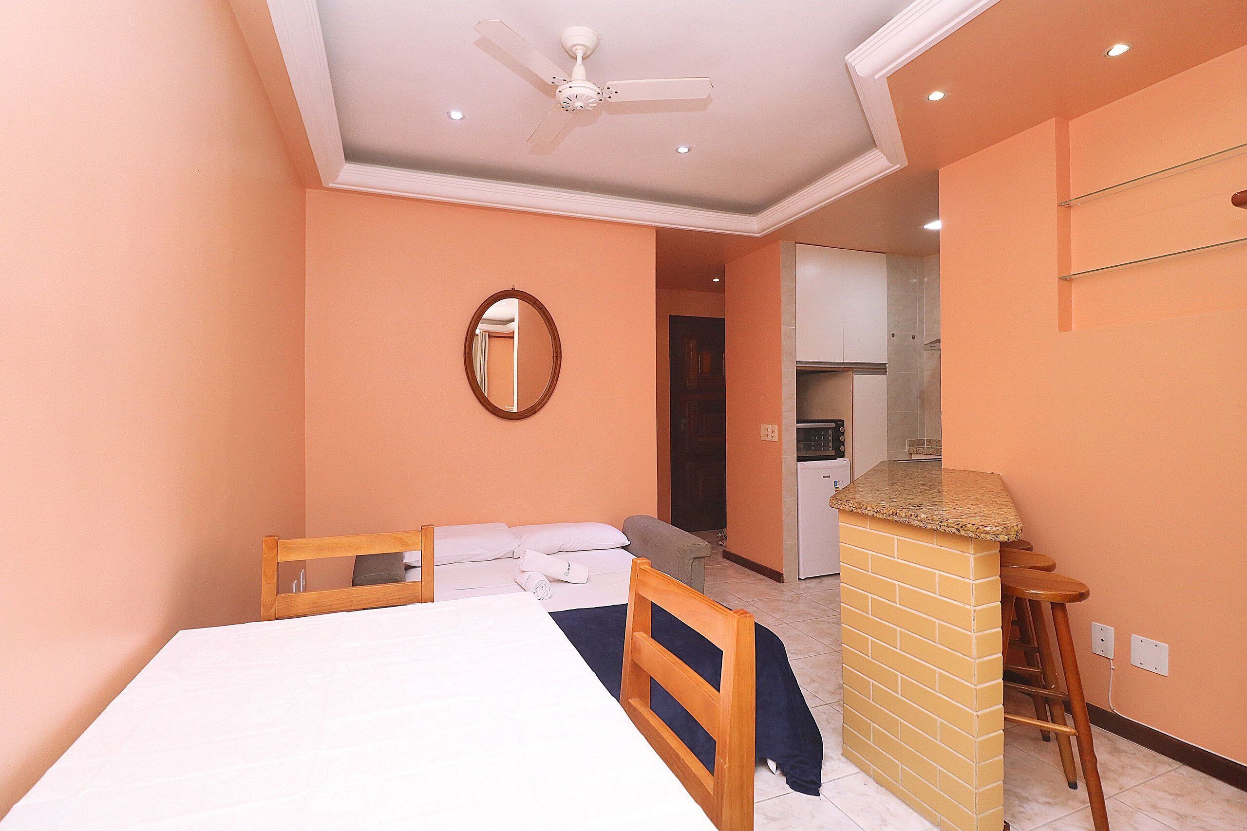 A hotel room with a bed, a wooden headboard, a small kitchen area, and a bathroom visible through an open door.