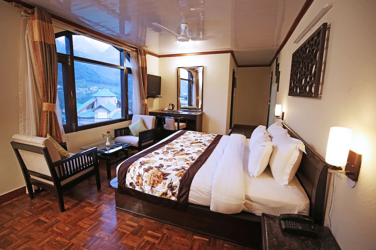 Habitación de hotel con una cama grande, un escritorio, una silla, un televisor y una ventana con cortinas.