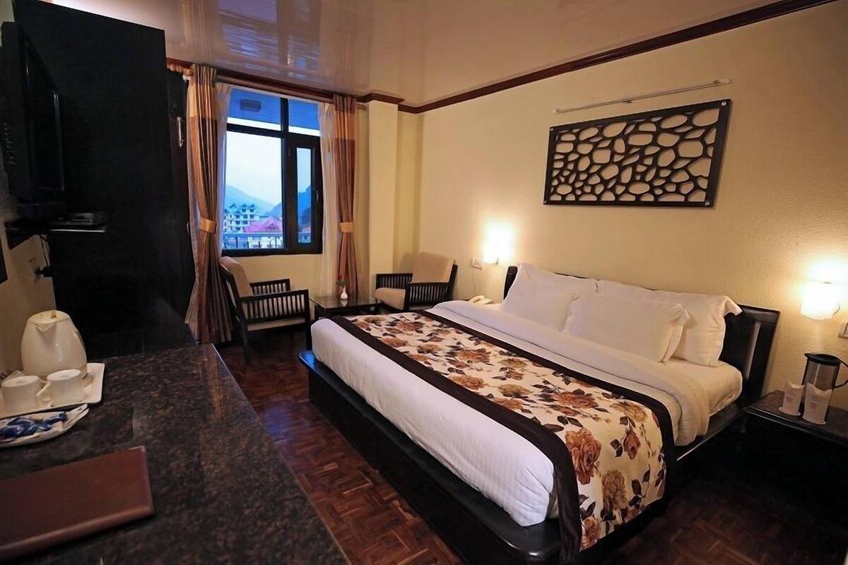 Habitación de hotel con cama, escritorio con silla, televisor y ventana con cortinas.