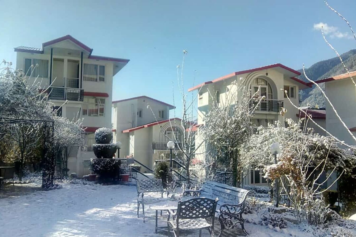 Un quartier résidentiel où le sol et les bâtiments sont recouverts de neige. On aperçoit des bancs et un élément décoratif sphérique dans le premier plan.