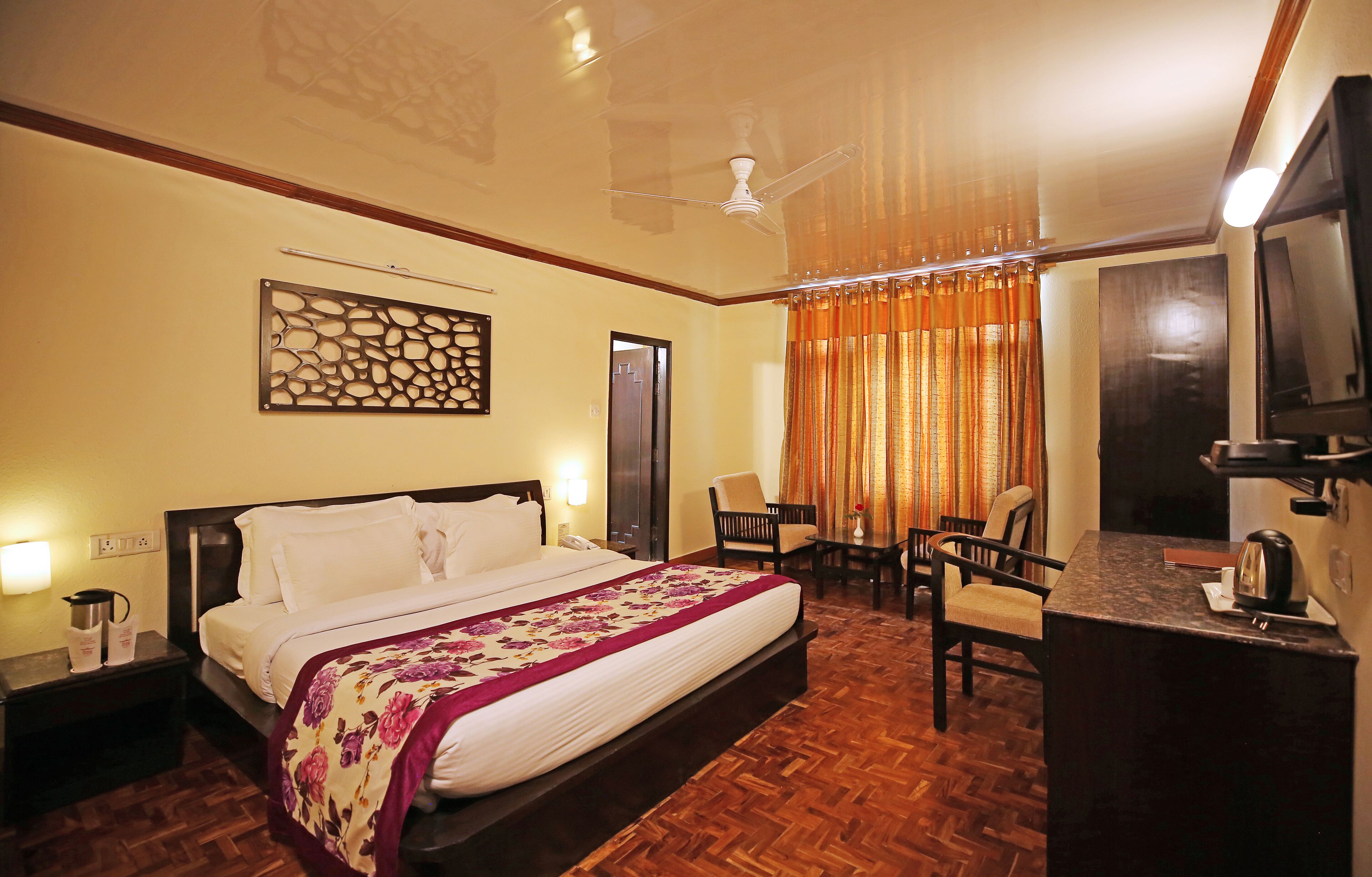 A hotel room with a large bed, a desk with a mirror, a chair, and a ceiling fan.