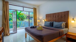 A bedroom with a large bed, wooden headboard, and a view of a garden through a sliding glass door. - The Baga Village (Baga)