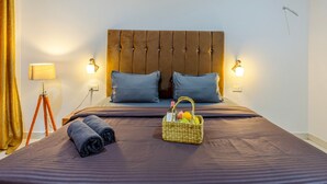 A neatly made bed with a headboard, two pillows, a rolled towel, and a basket with fruits. - The Baga Village (Baga)