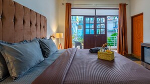 A hotel room with a large bed, a wooden headboard, a nightstand with a lamp, and a view of the outside balcony. - The Baga Village (Baga)
