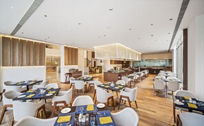 Un espace de restauration moderne doté de plusieurs tables et chaises, d’un bar central et d’un élément décoratif au plafond.