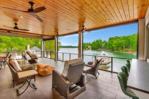 A covered outdoor area with wicker furniture, a view of a lake, and ceiling fans.