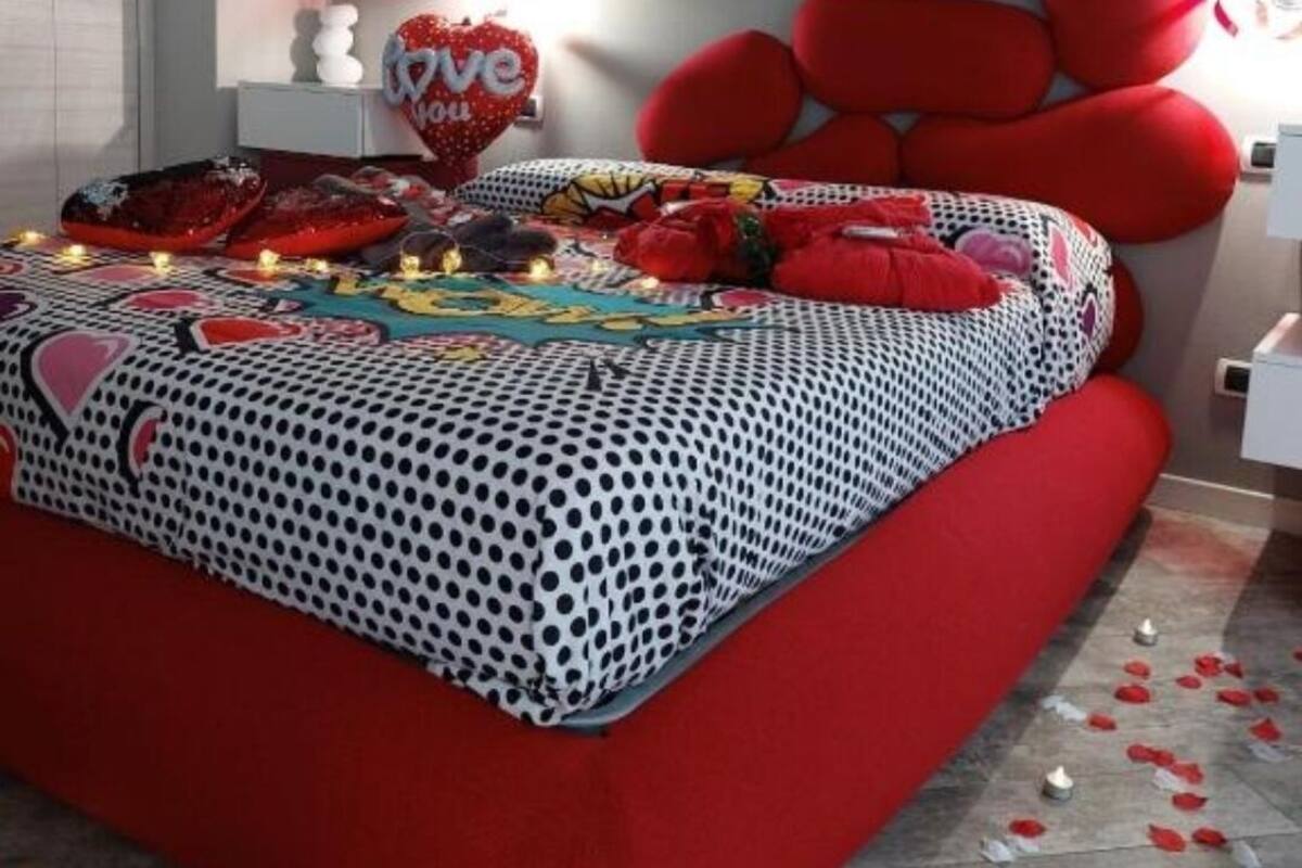 Een slaapkamer met een rood-wit bedsprei, een hartvormig kussen en een hartvormige decoratie aan de muur.