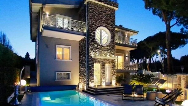 A modern two-story house with a swimming pool, stone facade, and outdoor seating area.
