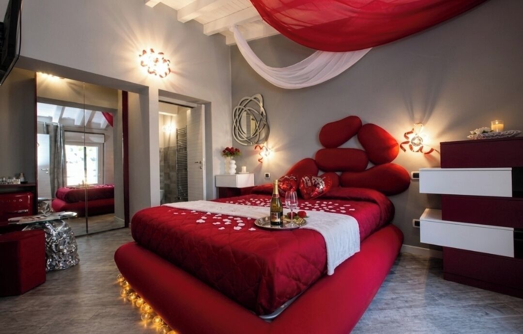 Una camera da letto moderna con un letto grande, biancheria rossa, un lampadario e uno specchio.