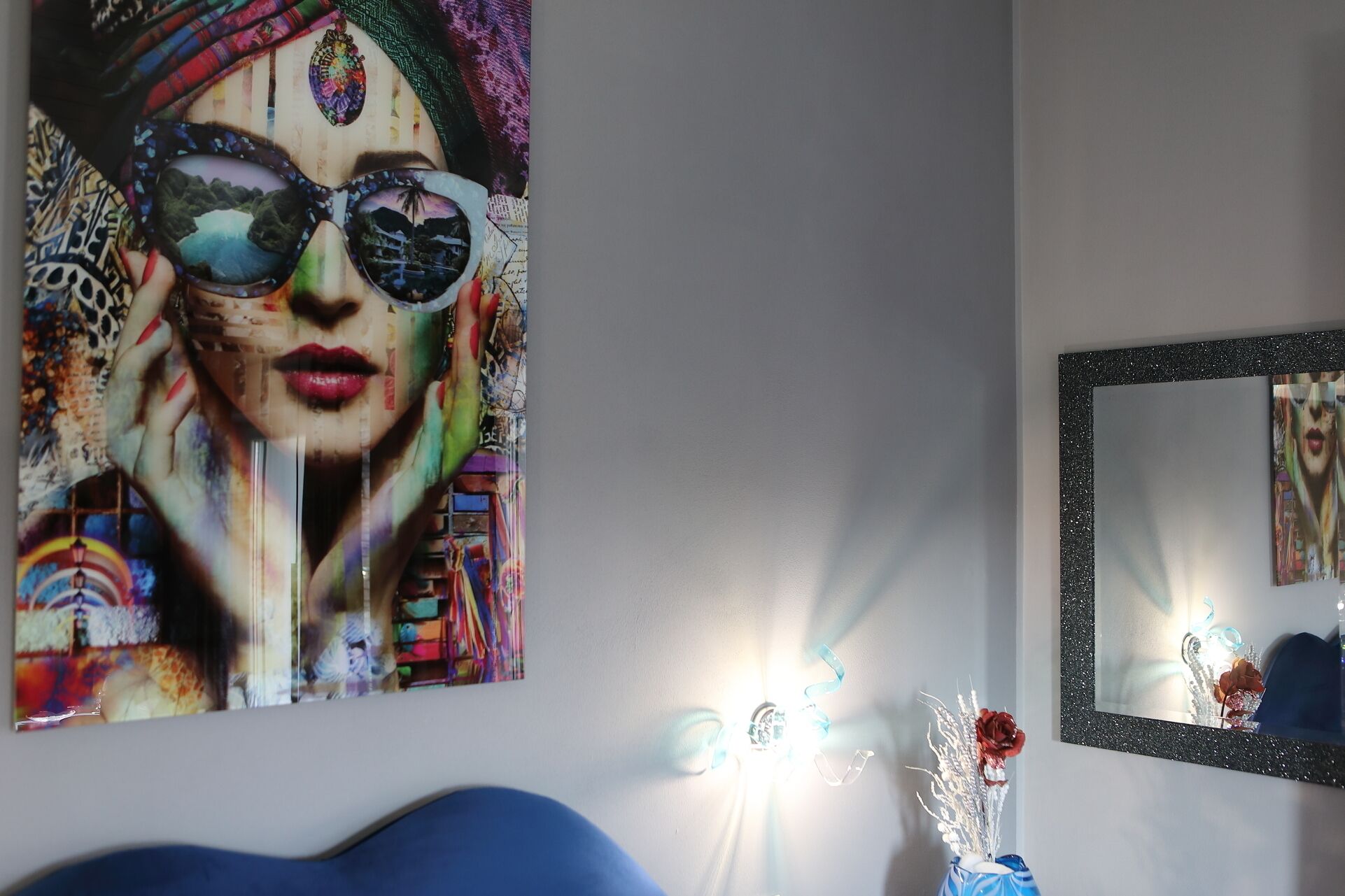 Una habitación con un cuadro abstracto grande, un espejo y un jarrón con plantas secas.