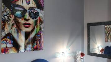 Una habitación con un cuadro abstracto grande, un espejo y un jarrón con plantas secas.