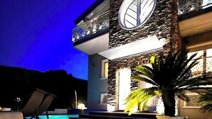 A modern house with a stone facade, a large circular window, and a pool area.
