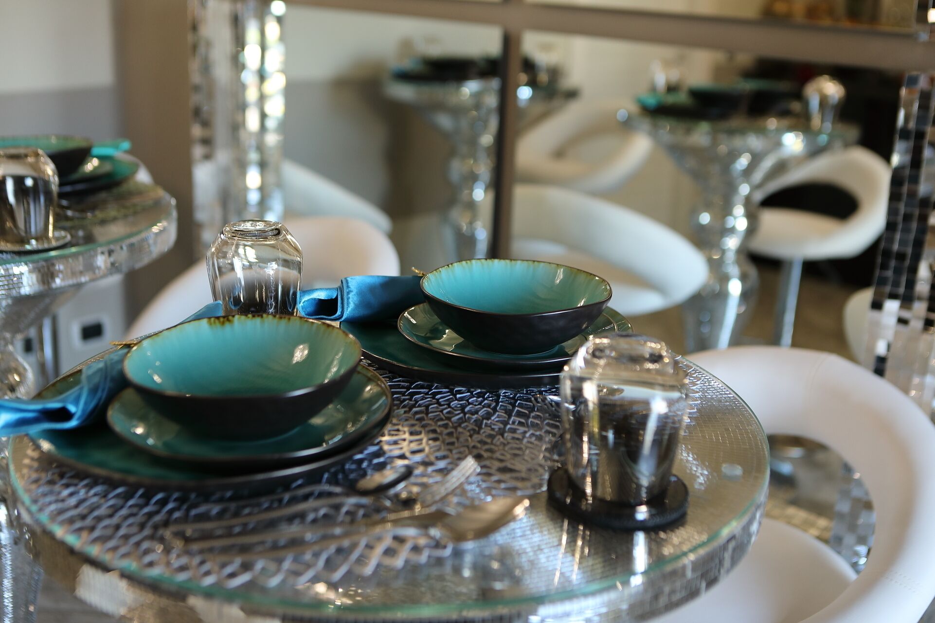 Un espace repas comprenant plusieurs tables rondes, chacune dotée d’un plateau en verre et d’un bol bleu-vert.