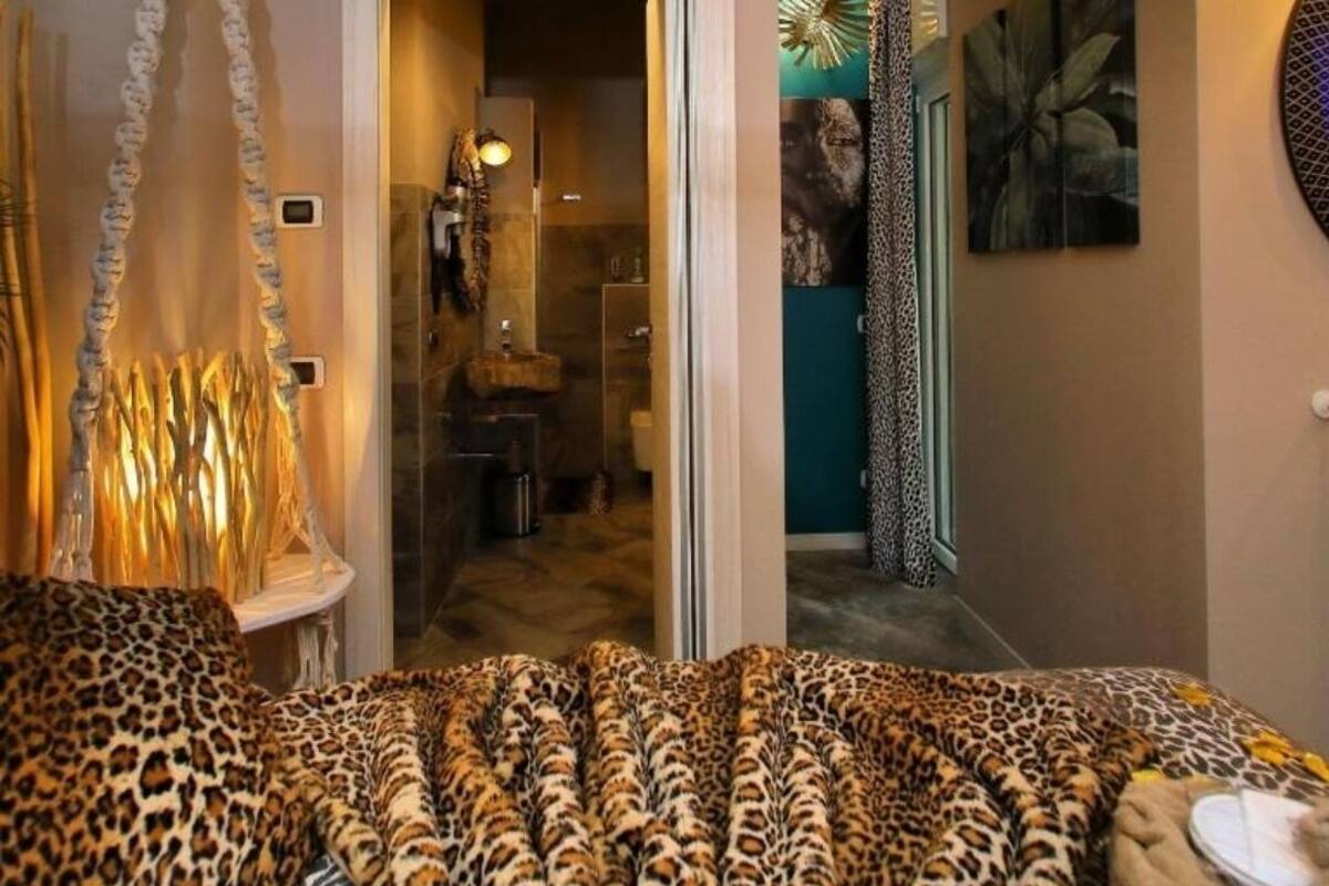 Een slaapkamer met een luipaardprint beddeken, een hangstoel en uitzicht op de badkamer en gang.