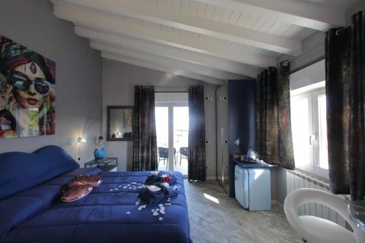Een slaapkamer met een bed, een bureau, een stoel en een groot raam met gordijnen.
