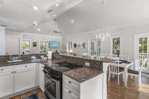 Una cocina moderna con encimeras de granito, muebles blancos y un comedor con sillas blancas.