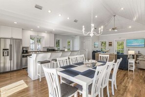 Una cocina moderna con armarios blancos, un refrigerador de acero inoxidable y un comedor con una mesa y sillas blancas.