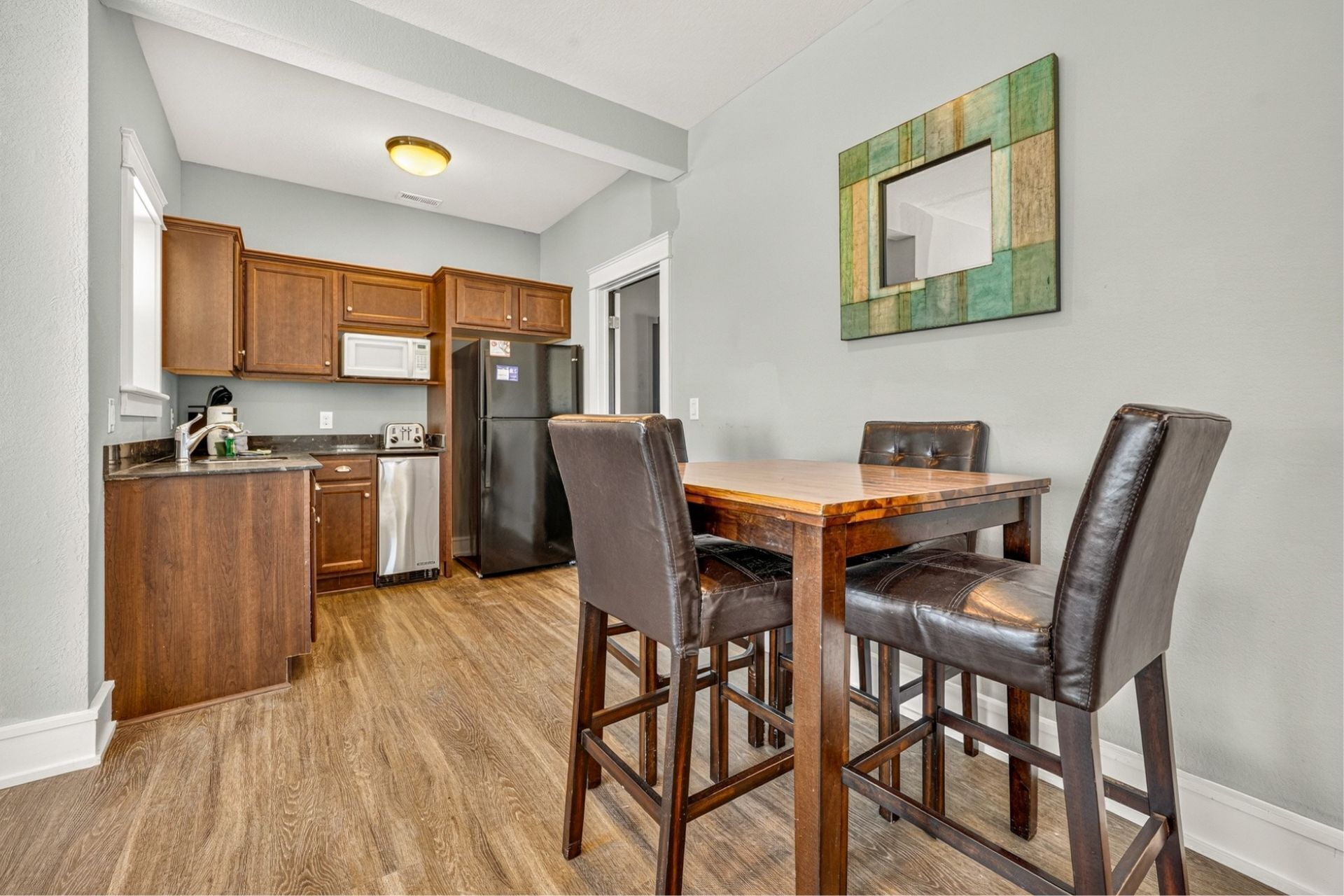 A kitchen with wooden cabinets, a refrigerator, a microwave, and a dining table with chairs.
