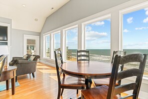Un espace repas avec une table et des chaises en bois, de grandes fenêtres donnant sur la plage et un aménagement intérieur moderne.