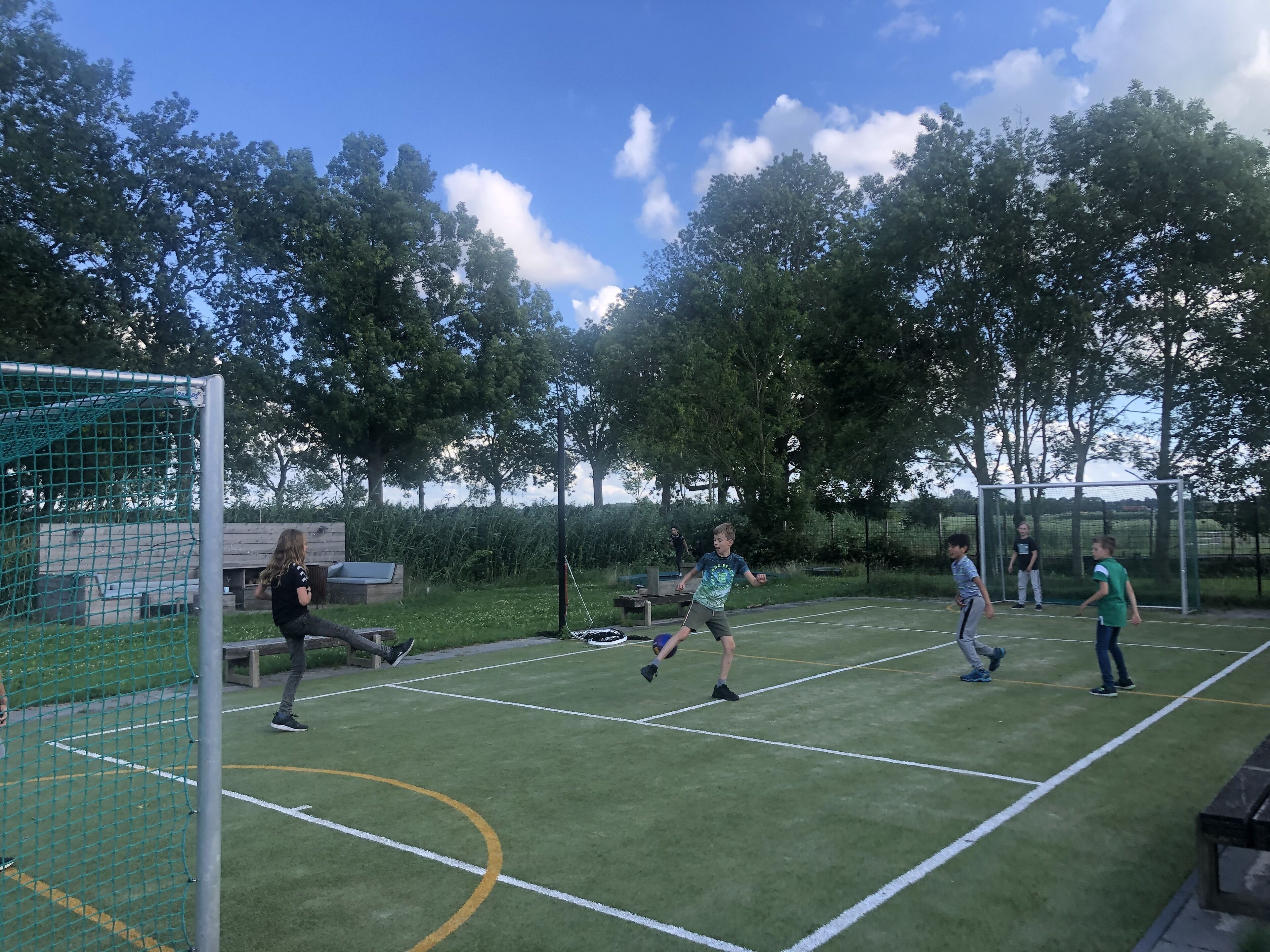 An outdoor sports field with a goalpost, surrounded by trees and a clear sky.