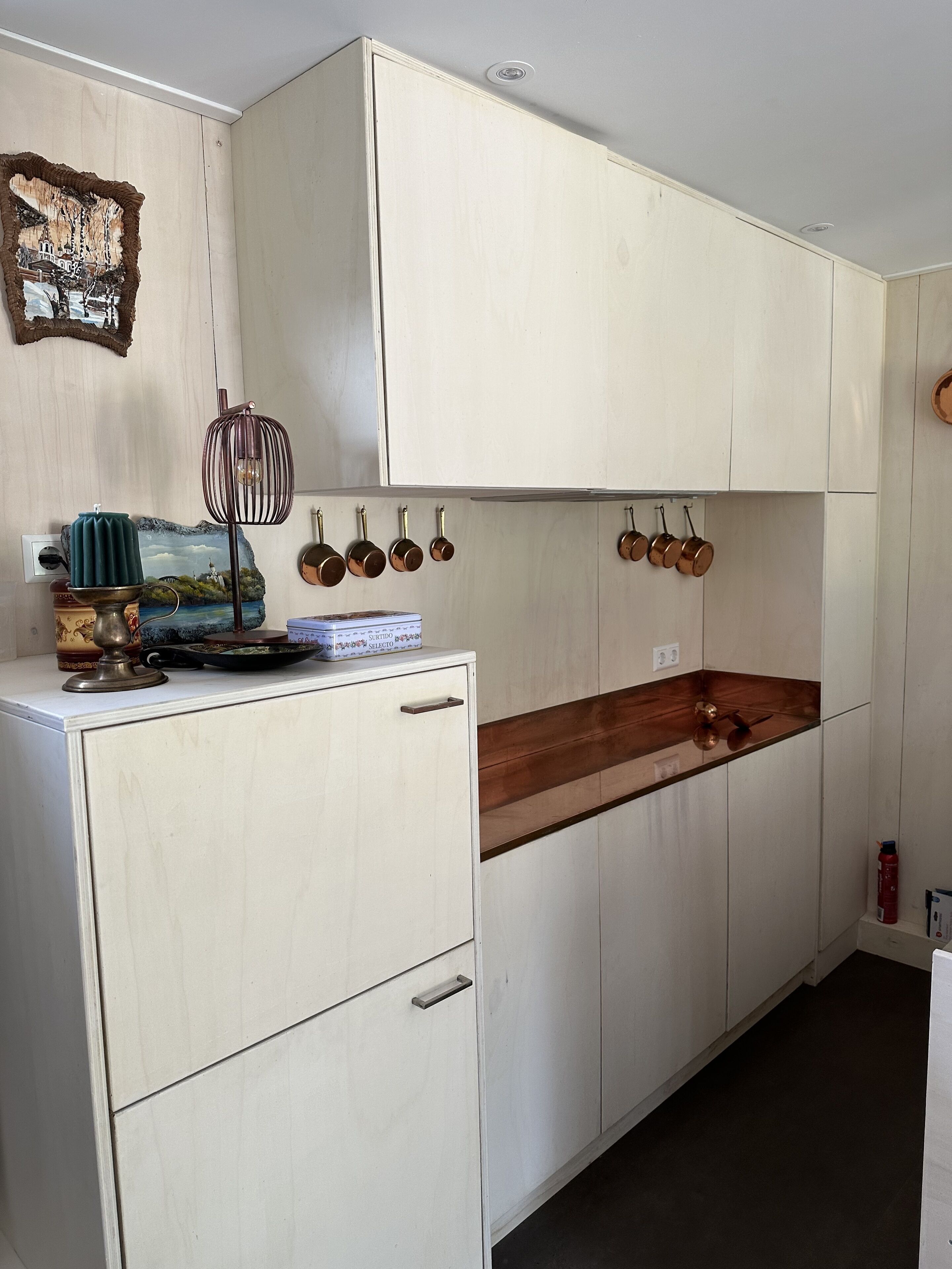 Una cocina con armarios blancos, encimera de madera y ollas de cobre colgando.
