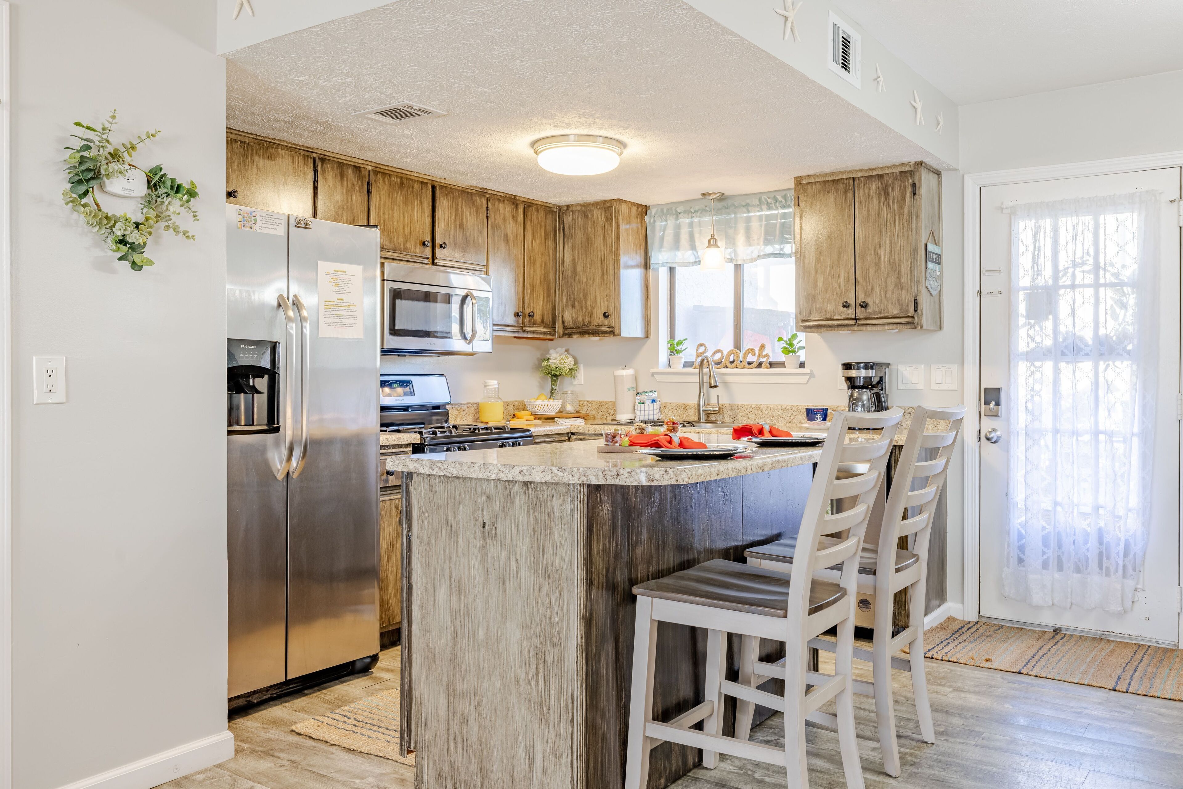 A kitchen with wooden cabinets, a stainless steel refrigerator, a microwave, a sink, and a bar area with stools.