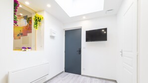 A modern bathroom with a skylight, a wall-mounted TV, and a door with a dark frame. - GLM Residences 2 (Saint-Quentin)