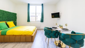 A modern bedroom with a bed, a TV mounted on the wall, and a dining area with a table and chairs. - GLM Residences 2 (Saint-Quentin)