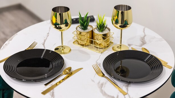 A table set with black plates, gold cutlery, and gold glasses, with two small potted plants in a gold holder. - GLM Residences 2 (Saint-Quentin)
