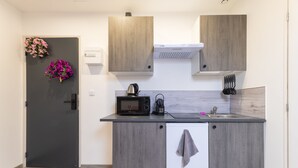 A compact kitchen with a microwave, kettle, and sink. There is a small cabinet with a towel hanging on it. - GLM Residences 2 (Saint-Quentin)