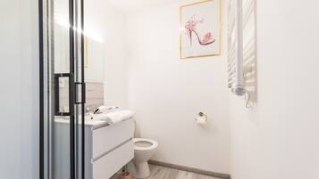 A modern bathroom with a glass shower enclosure, a white toilet, and a sink with a towel.