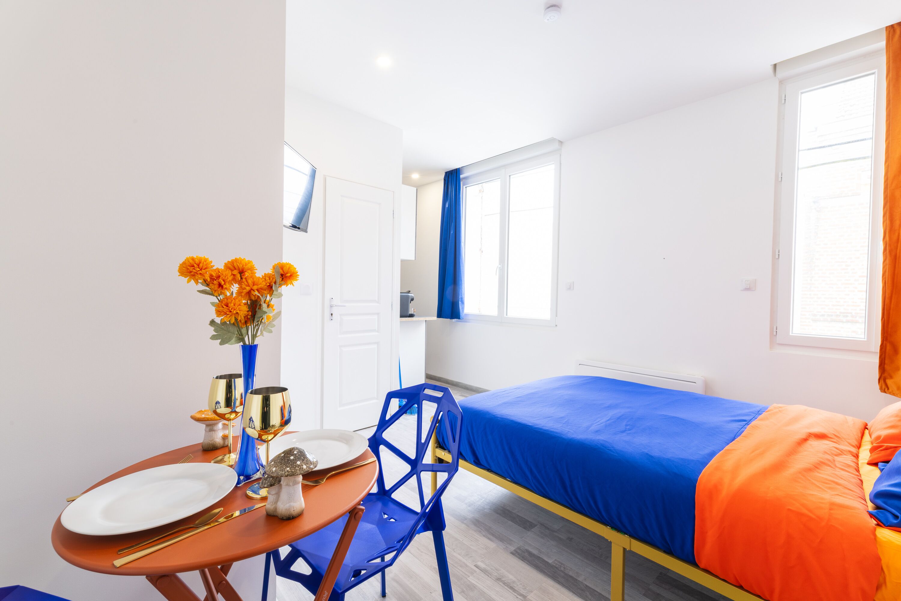 A compact hotel room with a single bed, a small table with a vase of flowers, and a chair.