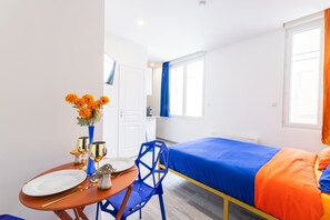 A compact hotel room with a single bed, a small table with a vase of flowers, and a chair. - GLM Residences 2 (Saint-Quentin)