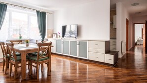 A modern kitchen with wooden cabinets, a dining table with chairs, and a television on the wall. - RentPlanet - Apartament Odrzańska (Wroclaw)