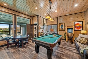A pool table, a billiards table, a pool cue, a sofa, and a chair in a room with wooden walls and ceiling. - 8 Bedroom ~Mtn View~ Sleeps 22 ~ Private Pool! (Sevierville)