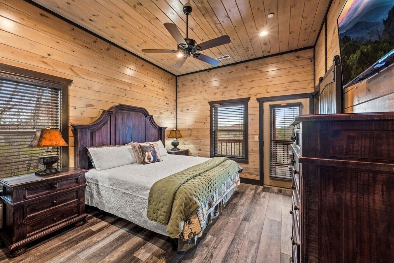 A wooden-paneled bedroom with a bed, nightstands, a dresser, and a ceiling fan.