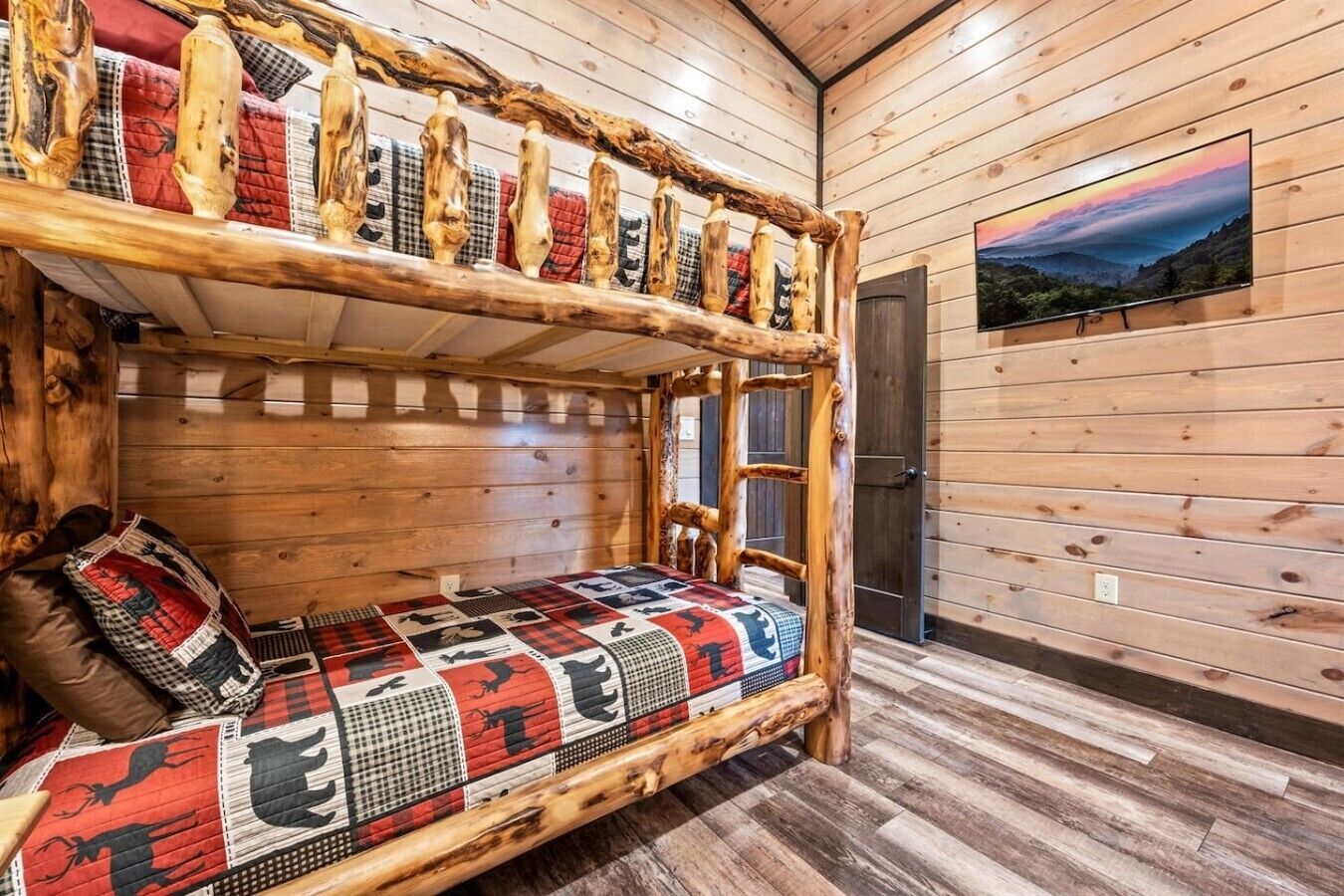 Un lit superposé avec une couverture matelassée, un mur en bois et un téléviseur fixé au mur.