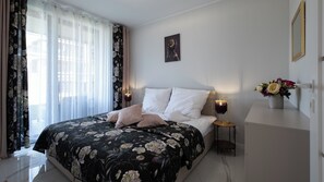 A neatly arranged bedroom with a floral bedspread, a bedside table with a lamp, and a vase with flowers. - Apartamenty Sun & Snow Żeglarska (gmina Lodygowice)