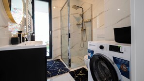 A modern bathroom with a glass-enclosed shower, a washing machine, and a marble-tiled floor. - Apartamenty Sun & Snow Żeglarska (gmina Lodygowice)
