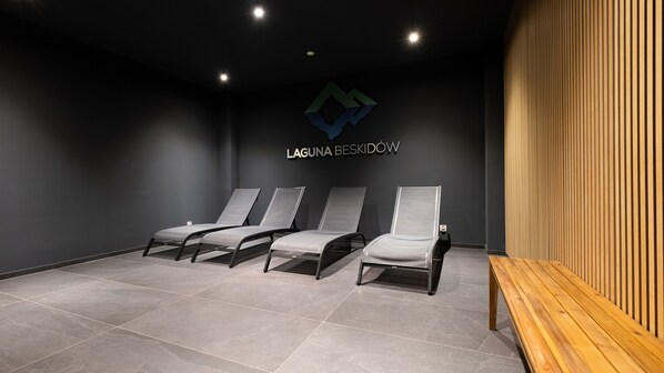 A modern waiting area with three reclining chairs, a wooden bench, and a logo on the wall.