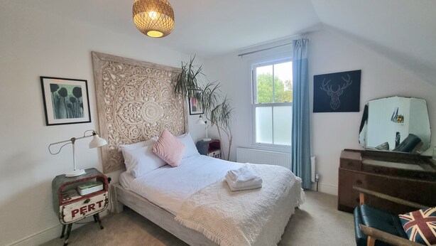 Une chambre à coucher avec un grand lit, une table de chevet avec une lampe, un miroir et une fenêtre avec des rideaux.